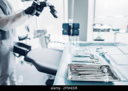 Sterile surgical instruments against background of nurse preparing medical equipment for dental surgery operation