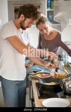 beautiful young caucasian beardy guy with curly hair making breakfast, while his female partner observing Stock Photo