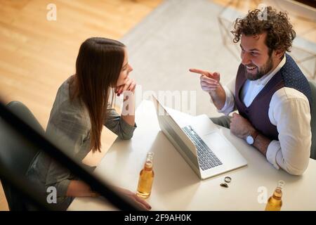 top view of young beardy caucasian male with curly hair smiling, pointing with index finger at his female colleague. Casual work from home due covid 1 Stock Photo