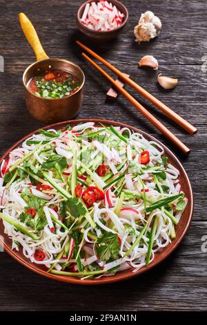 Rice noodle and vegetable salad on a plate on a wooden table with ...