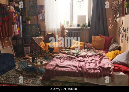Interior of old-fashioned domestic room with clothes on the rack and tray with bottle of red wine on the floor Stock Photo