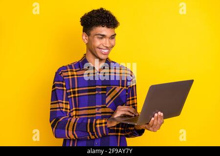 Photo portrait of young man working on laptop smiling isolated bright yellow color background Stock Photo