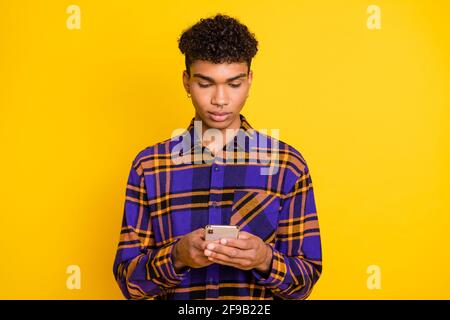 Photo portrait of man typing message on cellphone wearing checkered shirt isolated on vibrant yellow color background Stock Photo