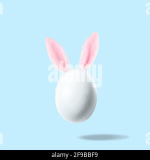 White egg with pink bunny ears against pastel blue background. Easter minimal concept. Creative Happy Easter or spring layout. Stock Photo
