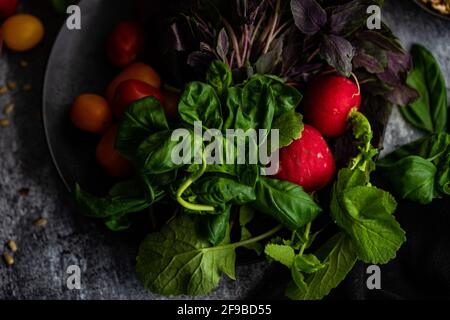 Healthy food concept with raw vegetables and herbs on black ceramic plate with seeds on dark stone background Stock Photo