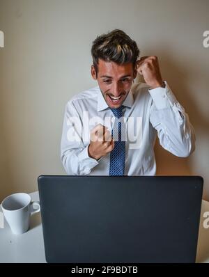 Closeup of Caucasian male beaming with excitement while looking at his laptop Stock Photo