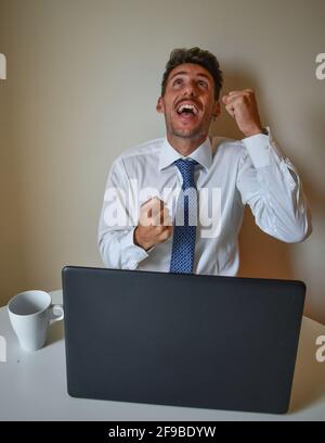 Excited young Caucasian businessman sitting in front of the laptop on the table Stock Photo