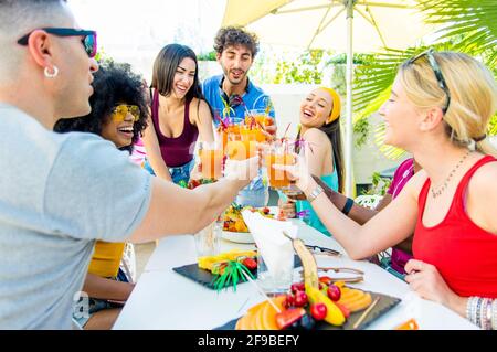 Multiracial friends having fun in backyard home party - Friendship concept with young people toasting cocktails at bar restaurant - Focus on glasses Stock Photo