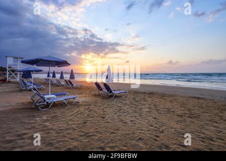 Unbelievable sunrise. Empty beach with umbrellas and deck chairs closed. Beautiful summertime view seascape. Morning landscape. High waves with foam. Stock Photo