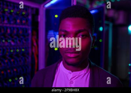 Portrait of serious young African-American data center engineer standing against server cabinet in dark room Stock Photo