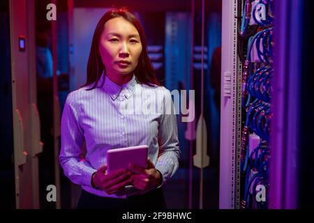 Portrait of serious confident Asian computer network engineer using tablet while checking productivity of servers Stock Photo