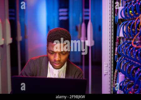 Busy young black IT engineer using modern laptop in server room while administrating computer network Stock Photo