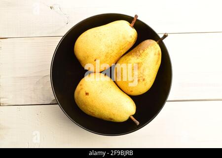 Five juicy pears, in a black ceramic plate, on a painted wooden table. Stock Photo