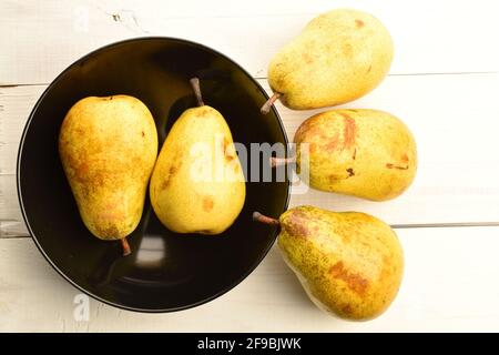 Five juicy pears, in a black ceramic plate, on a painted wooden table. Stock Photo