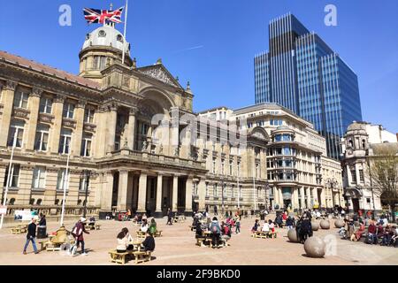 Birmingham city centre, UK. 17th Apr, 2021. Shoppers and revellers sat on benches outside Birmingham Council House with the Union Flag flying at half mast after the death of Prince Philip. Visitors took advantage of the beautiful weather in Birmingham city centre to enjoy 'Super Saturday'. Thousands of people came out despite the funeral of Prince Philip taking place today. Pubs and bars were full and streets were a sea of people. Pic by Credit: Ben Formby/Alamy Live News Stock Photo