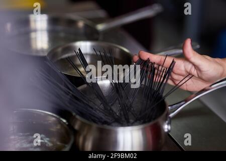 nera pasta is manually dipped in a pot of boiling water in the kitchen Stock Photo