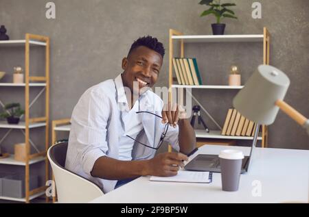 Smiling black businessman looking at camera sitting at desk with laptop in home office Stock Photo
