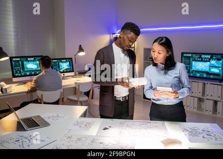 Busy multi-ethnic vehicle designers standing with maquette and tablet and working on new model of car in modern office Stock Photo