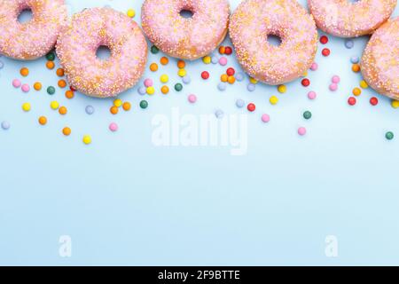 Pink doughnuts and candies on blue background, copy space flat lay Stock Photo