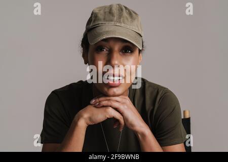 Joyful african american soldier woman smiling while sitting on chair isolated over grey wall Stock Photo