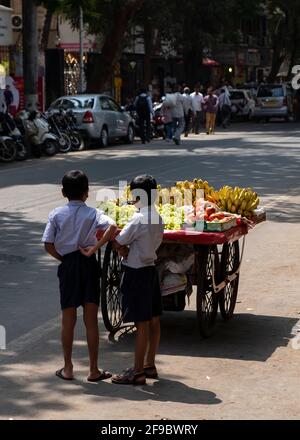 Two school boys standing near a fruit sellers cart waiting for the vendor in the Mumbai suburb of Dadar,Maharashtra, India,Asia. Stock Photo