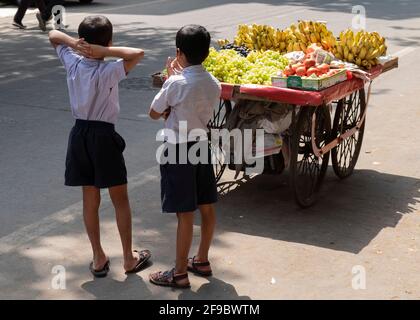 Two school boys standing near a fruit sellers cart waiting for the vendor in the Mumbai suburb of Dadar,Maharashtra, India,Asia. Stock Photo