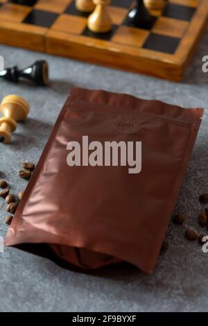 Blank coffee packaging with degassing valve, coffee beans and chess, coffee packaging mockup with empty space to display your branding design. Stock Photo