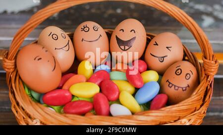 Stack of eggs with hand drawn faces on straw basket with colorful candy, easter preparation, holiday mood concepts Stock Photo