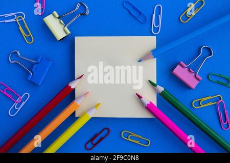 Top view of the empty blank  for writing, color pencils and clips  on the blue background.Copy space. Stock Photo