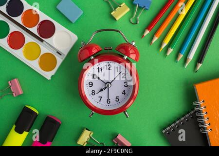 Red alarm clock  and school stationery  on the green background.Top view. Stock Photo
