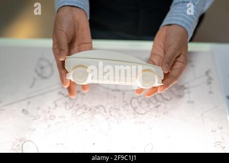 Close-up of unrecognizable woman holding white model of car above sketch in office Stock Photo