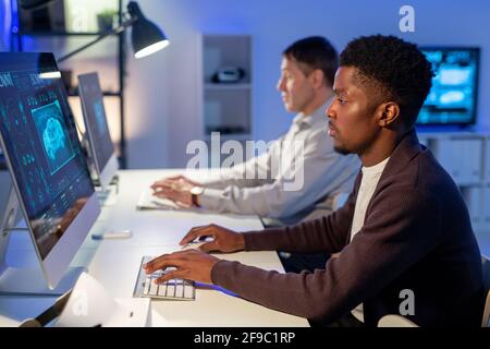 Side view of concentrated young African American engineer sitting at desk and drawing car model on computer Stock Photo