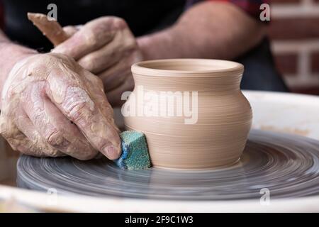 Male hands cleaning with sponge pottery on a potter wheel. The final stage of manufacture of the bowl Stock Photo
