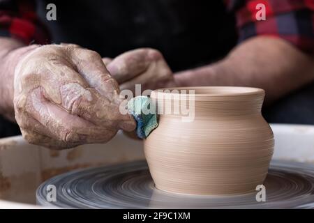 Male hands cleaning with sponge pottery on a potter wheel. The final stage of manufacture of the bowl Stock Photo