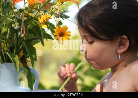 Summer vacation in the village. Little girl drinks water from a glass through a straw outdoors Stock Photo