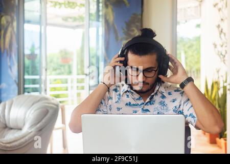 Hispanic man adjusting his headphones while working on his computer at home in quarantine Stock Photo