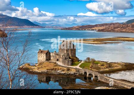 EILEAN DONAN CASTLE LOCH DUICH HIGHLANDS SCOTLAND BLUE SKY AND A BLUE LOCH IN SPRING  MOUNTAINS IN THE DISTANCE SALTIRE FLAG AT HALF MAST Stock Photo