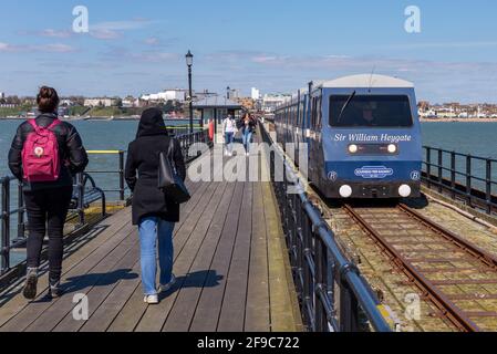 Southend on Sea, Essex, UK. 17th April, 2021. The day has been bright and sunny in the seaside town, but with a chill wind. Many people have visited to enjoy the seafront and its famous pier. People walking on the walkway as the pier train passes Stock Photo