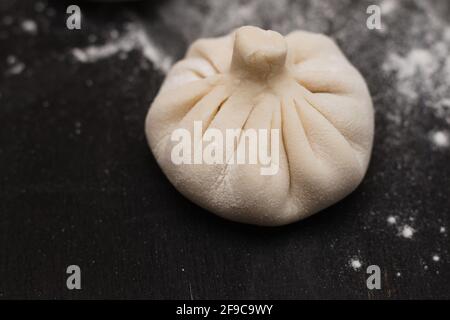 Single raw Georgian khinkali on a black wooden table Stock Photo