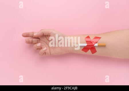 A cigarette glued with a cross to a woman's hand, quit smoking concept. Stock Photo