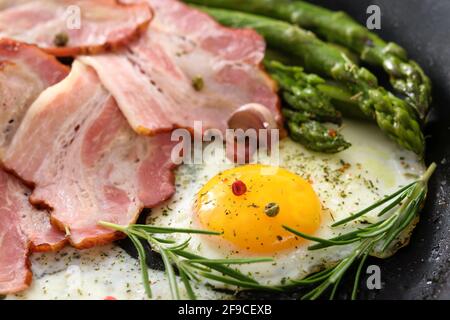 Fried asparagus with bacon, eggs and spices on a pan in close-up Stock Photo