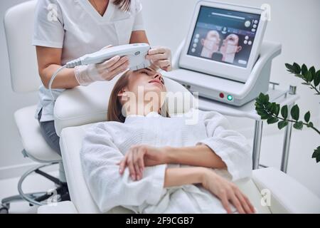 Happy beautiful female client receiving professional vacuum face massage in medicine clinic Stock Photo
