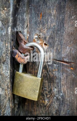 close up of a closed padlock on an antique wooden door with rusted metal fittings, vertical Stock Photo