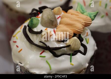 Freshly prepared Easter cakes in paper forms, decorated with fondant, chocolate icing and sugar eggs and carrots Stock Photo