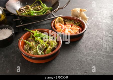 Spanish tapas, fried pimientos or padron peppers and shrimps in traditional bowls on a dark gray slate background, copy space, selected focus, narrow Stock Photo