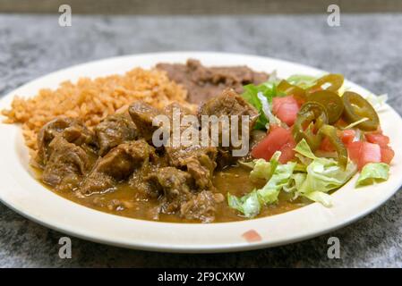 Authentic Mexican food plate of chili verde pork smothered in green sauce served with refried beans and rice. Stock Photo