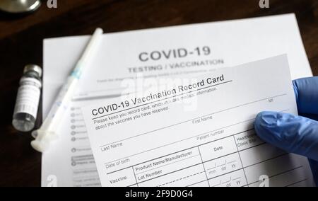 COVID-19 Vaccination Record Card in doctor hand, coronavirus test and vaccine medical form on desk in clinic. Concept of corona virus vaccination cert Stock Photo