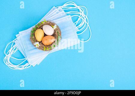 Nest with brightly dyed eggs with medical masks on blue background, space for text. Easter holiday during the Coronavirus pandemic. Studio Photo Stock Photo