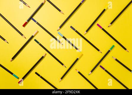 Colored pencils are graphically laid out on a yellow background, top view, hard shadows. Abstraction Stock Photo