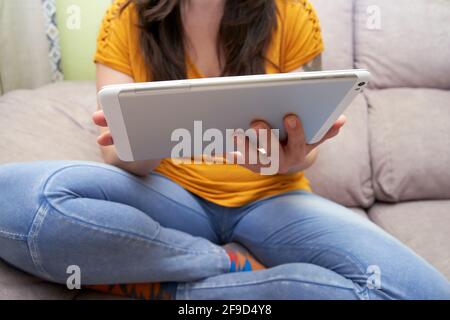 A cropped young woman in casual clothes uses a digital tablet while working from home. Concept of teleworking, gadgets, comfort, lifestyle. Stock Photo